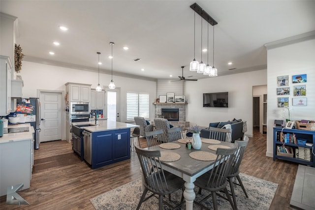 dining space with sink, crown molding, dark hardwood / wood-style floors, ceiling fan, and a fireplace