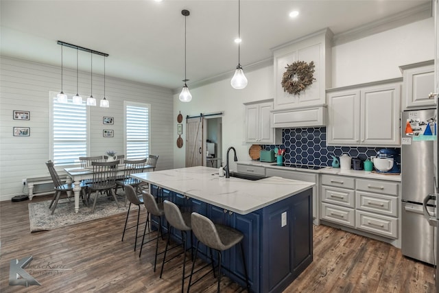 kitchen with sink, a center island with sink, stainless steel fridge, a barn door, and light stone countertops