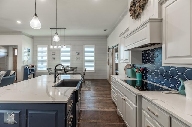 kitchen featuring sink, a center island with sink, black electric cooktop, and decorative light fixtures