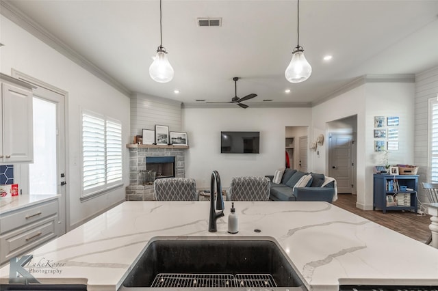 kitchen featuring light stone counters, sink, pendant lighting, and a fireplace