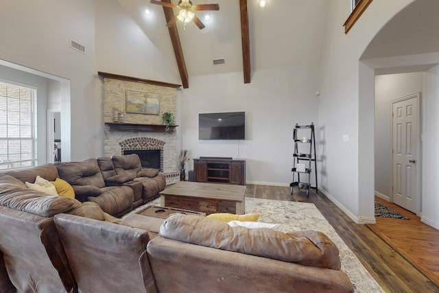 living room with dark wood-type flooring, a stone fireplace, high vaulted ceiling, beamed ceiling, and ceiling fan