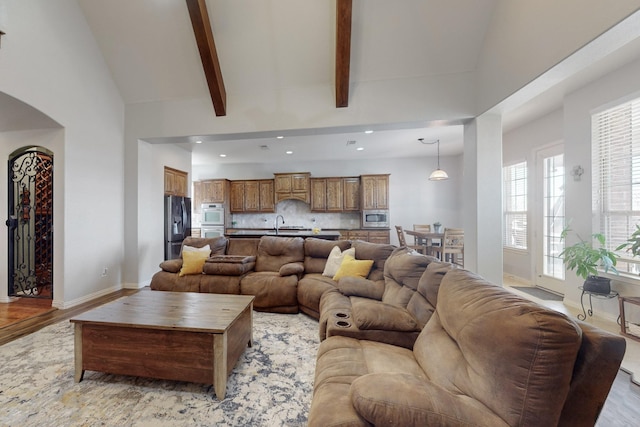 living room with sink, high vaulted ceiling, beamed ceiling, and light wood-type flooring