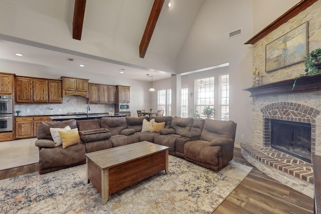 living room with beamed ceiling, high vaulted ceiling, sink, and light hardwood / wood-style flooring