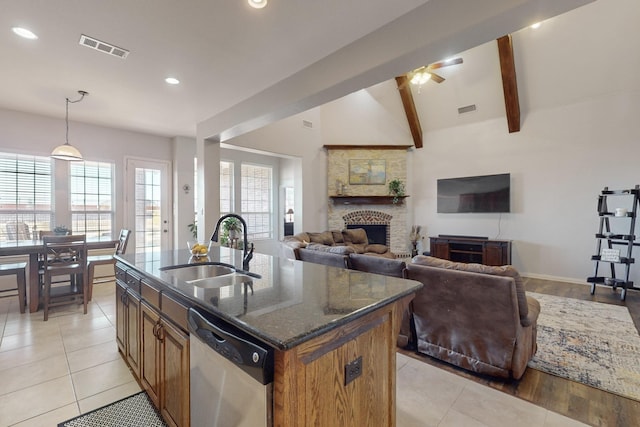 kitchen featuring a fireplace, an island with sink, sink, dark stone countertops, and stainless steel dishwasher