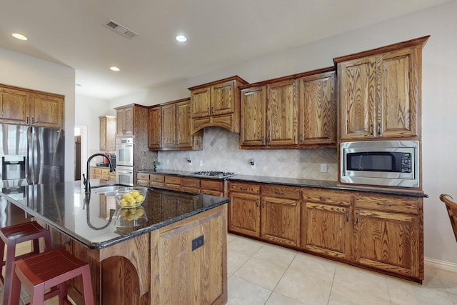 kitchen with stainless steel appliances, sink, a center island with sink, and dark stone counters