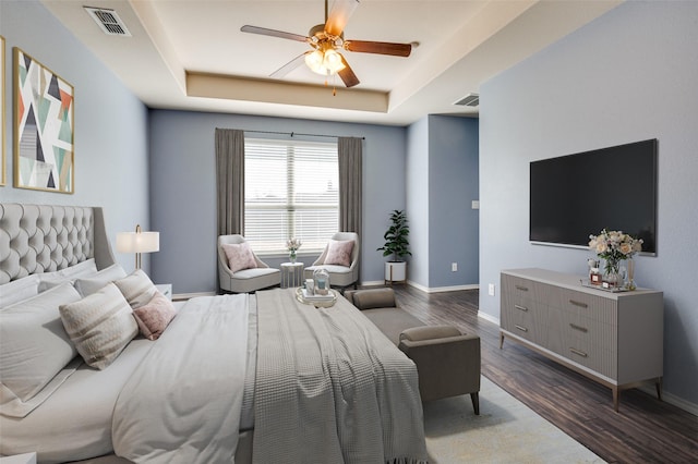 bedroom with a raised ceiling, visible vents, baseboards, and wood finished floors