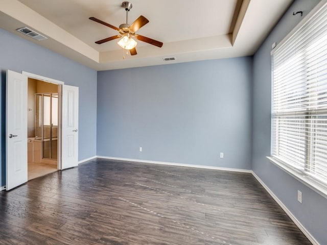 empty room with baseboards, visible vents, a raised ceiling, and wood finished floors