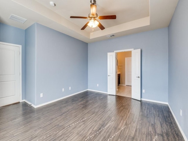 empty room featuring a tray ceiling, wood finished floors, visible vents, and baseboards