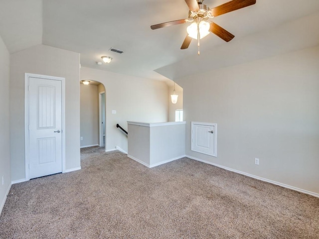 carpeted empty room with baseboards, visible vents, arched walkways, and ceiling fan