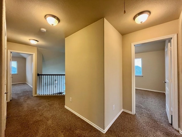 corridor with carpet floors, baseboards, and a textured ceiling