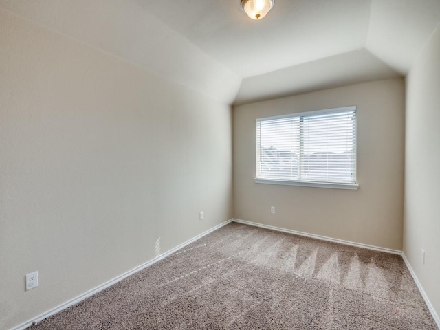 spare room featuring lofted ceiling, carpet, and baseboards