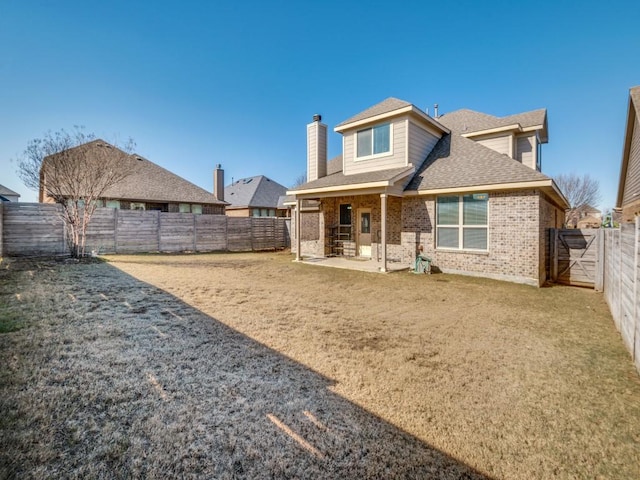 rear view of property featuring brick siding, roof with shingles, a chimney, a patio area, and a fenced backyard