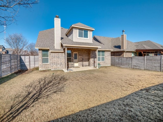 rear view of house featuring a patio, a fenced backyard, a chimney, roof with shingles, and brick siding