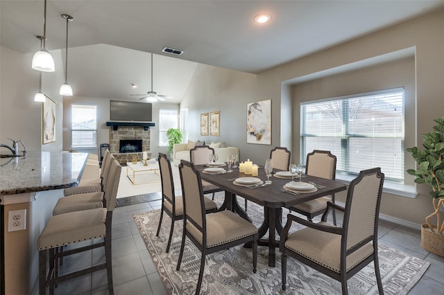 dining space with lofted ceiling, visible vents, a stone fireplace, and dark tile patterned flooring