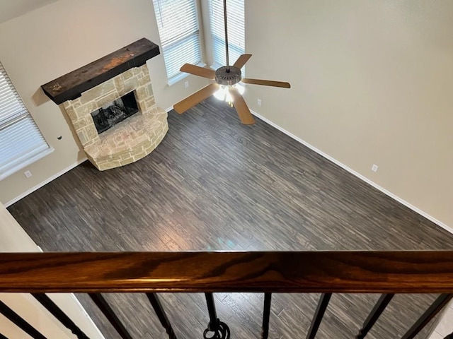 interior space featuring ceiling fan, a stone fireplace, wood finished floors, and baseboards