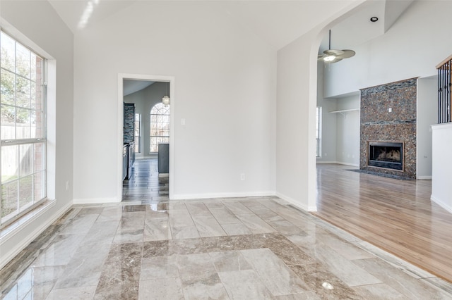 unfurnished living room featuring ceiling fan, high vaulted ceiling, a tile fireplace, and light wood-type flooring