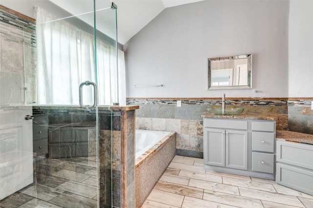 bathroom with lofted ceiling, vanity, independent shower and bath, and tile walls