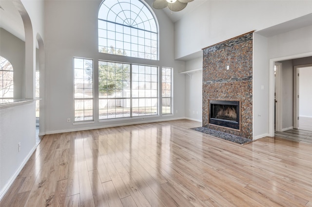 unfurnished living room with ceiling fan, a fireplace, light hardwood / wood-style floors, and a towering ceiling