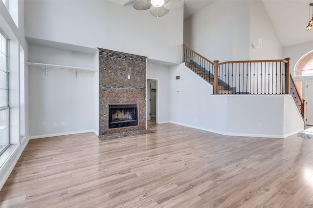 unfurnished living room with a fireplace, high vaulted ceiling, ceiling fan, and light wood-type flooring