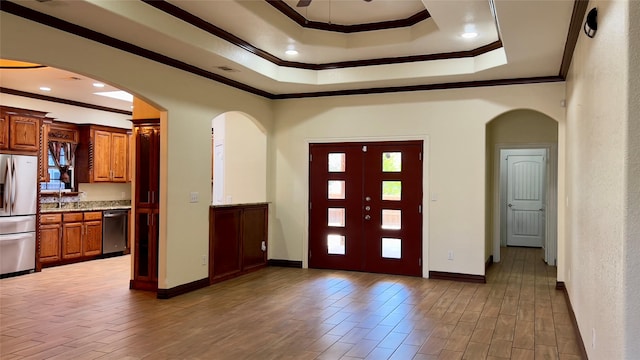 foyer entrance with wood-type flooring, ornamental molding, a raised ceiling, and ceiling fan