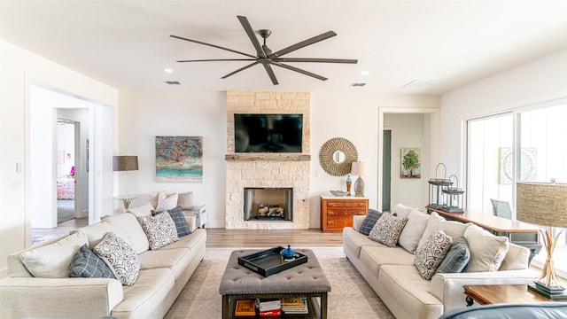 living room featuring ceiling fan, a stone fireplace, and light wood-type flooring