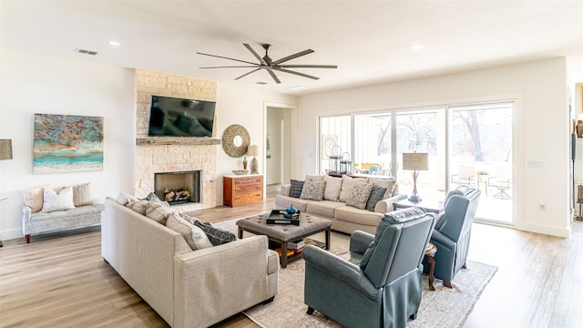 living room with a stone fireplace, ceiling fan, and light hardwood / wood-style flooring