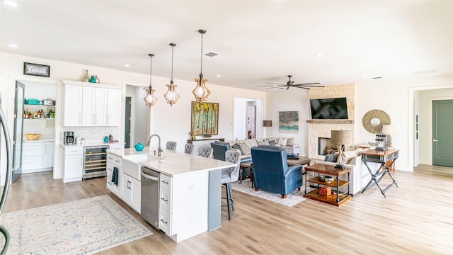 kitchen with sink, dishwasher, hanging light fixtures, white cabinets, and a center island with sink