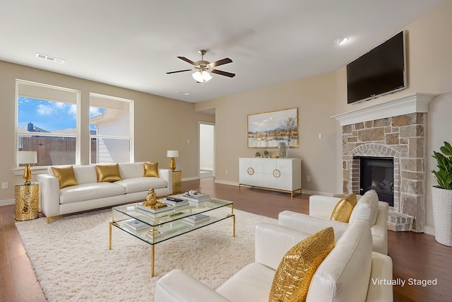 living room featuring a stone fireplace, dark hardwood / wood-style floors, and ceiling fan