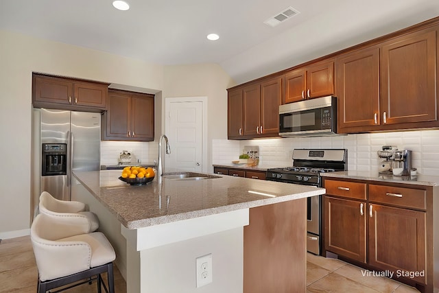 kitchen with a kitchen bar, sink, light tile patterned floors, appliances with stainless steel finishes, and an island with sink