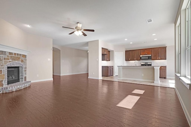 unfurnished living room featuring ceiling fan, a stone fireplace, and light wood-type flooring