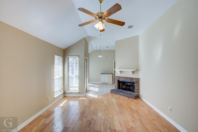 unfurnished living room featuring ceiling fan, lofted ceiling, a brick fireplace, and light wood-type flooring