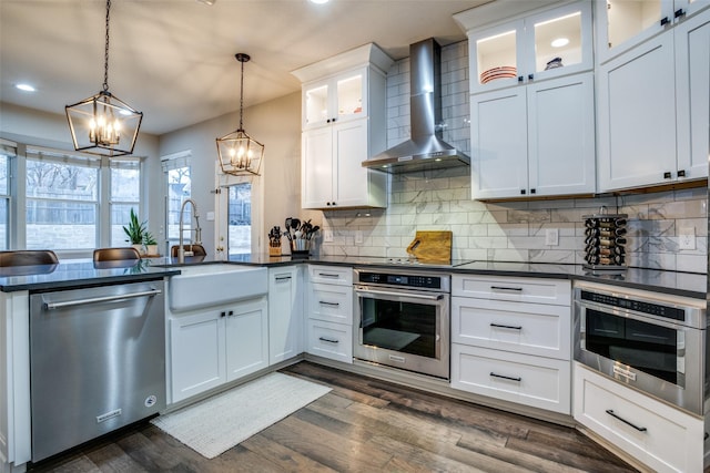 kitchen featuring pendant lighting, white cabinetry, sink, stainless steel appliances, and wall chimney range hood