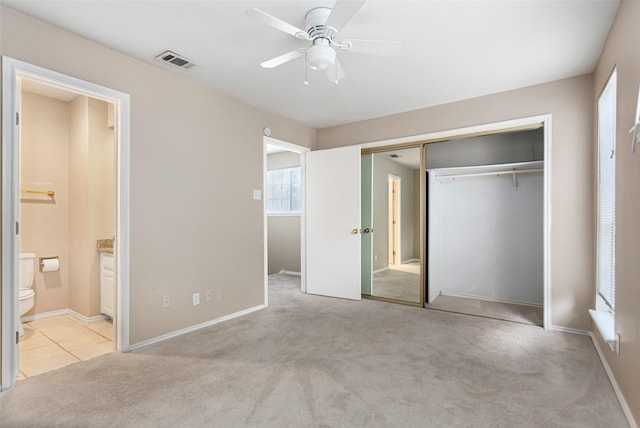 unfurnished bedroom featuring connected bathroom, light colored carpet, a closet, and ceiling fan