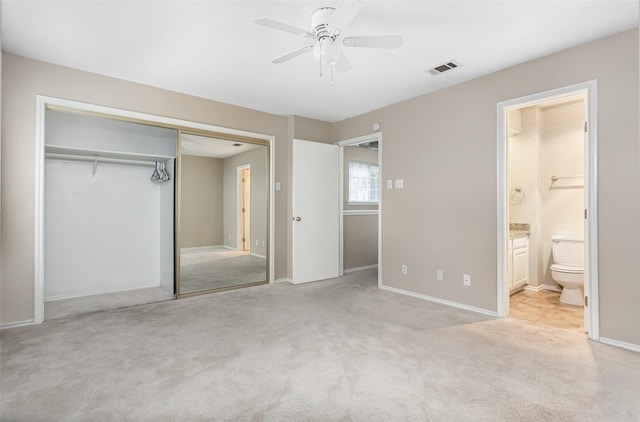 unfurnished bedroom featuring ensuite bathroom, light colored carpet, ceiling fan, and a closet