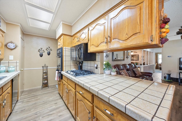 kitchen featuring light hardwood / wood-style flooring, backsplash, tile counters, ornamental molding, and black appliances