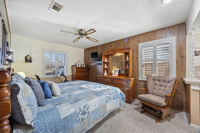 bedroom with ceiling fan, light carpet, a textured ceiling, and wooden walls