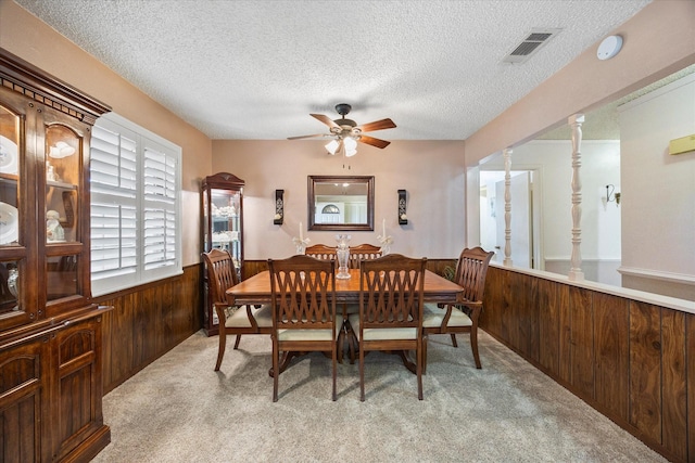 carpeted dining space featuring ceiling fan, wooden walls, a textured ceiling, and ornate columns