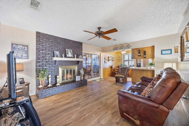 living room with ceiling fan, a fireplace, light hardwood / wood-style flooring, and a textured ceiling