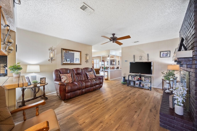 living room with hardwood / wood-style floors, a textured ceiling, a brick fireplace, and ceiling fan