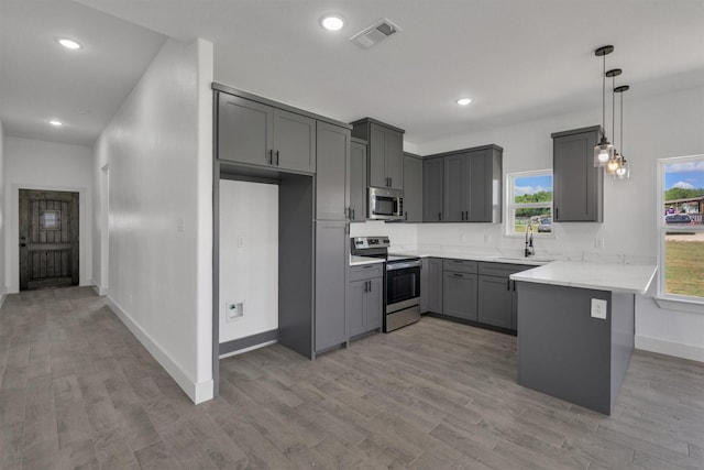 kitchen with sink, gray cabinetry, stainless steel appliances, decorative light fixtures, and kitchen peninsula