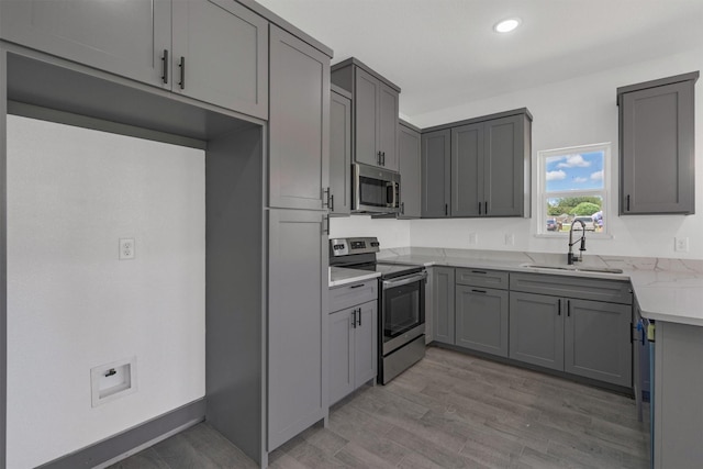 kitchen with stainless steel appliances, light stone countertops, gray cabinets, and sink