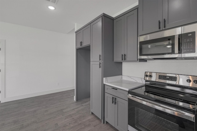 kitchen with gray cabinets, light stone countertops, appliances with stainless steel finishes, and light wood-type flooring