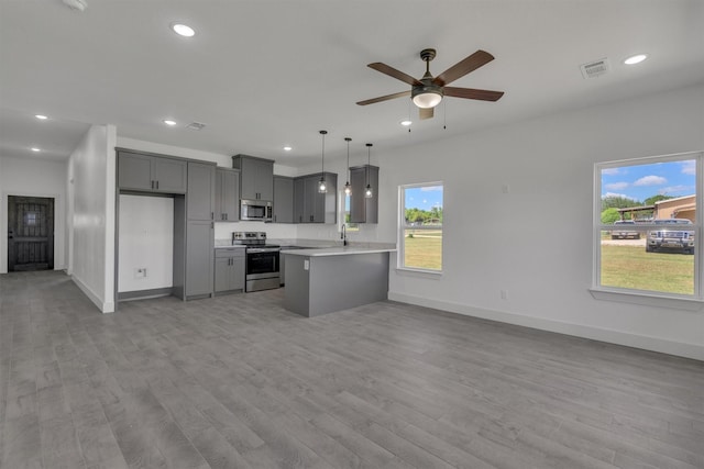 kitchen with pendant lighting, light hardwood / wood-style flooring, appliances with stainless steel finishes, gray cabinetry, and kitchen peninsula