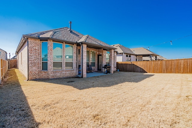 rear view of property with brick siding, roof with shingles, a fenced backyard, and a patio area