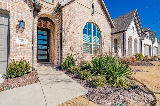 property entrance featuring brick siding, roof with shingles, and an attached garage