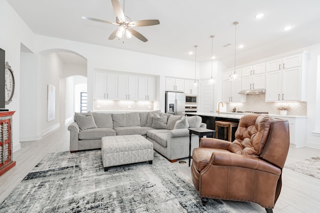 living room featuring light wood-type flooring, recessed lighting, arched walkways, baseboards, and ceiling fan