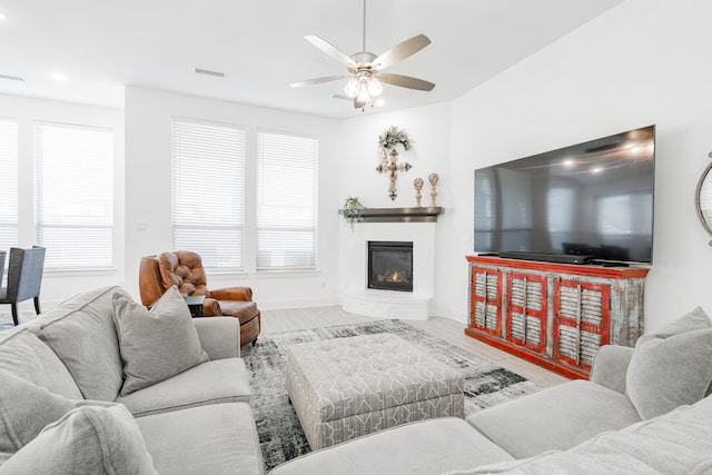 living area with wood finished floors, baseboards, visible vents, a ceiling fan, and a glass covered fireplace