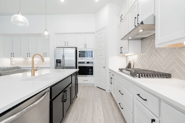 kitchen with under cabinet range hood, light countertops, appliances with stainless steel finishes, white cabinetry, and a sink