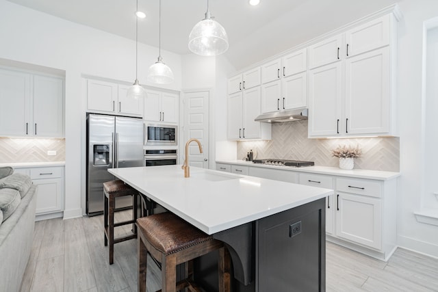 kitchen with under cabinet range hood, a kitchen bar, appliances with stainless steel finishes, white cabinets, and a sink