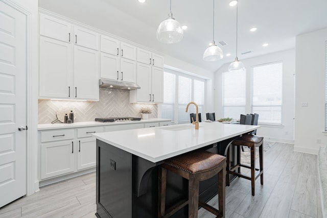 kitchen featuring a sink, under cabinet range hood, tasteful backsplash, light countertops, and cooktop